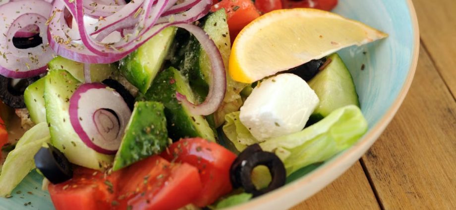 A vibrant bowl of Greek salad with fresh vegetables, feta cheese, and a lemon slice.